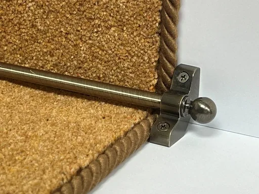Antique brass stair rod securing a beige carpet runner with rope binding.
