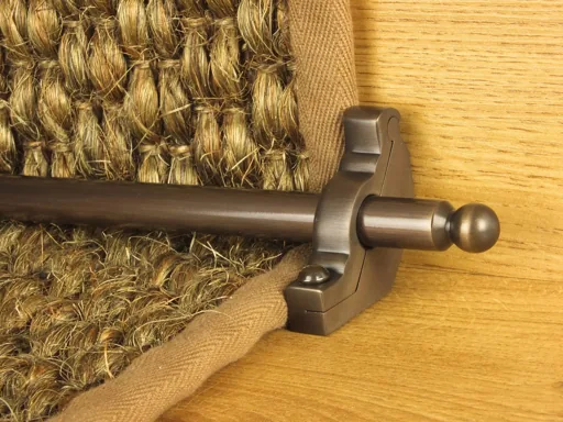 Antique brass stair rod securing a natural fiber runner with brown fabric binding.