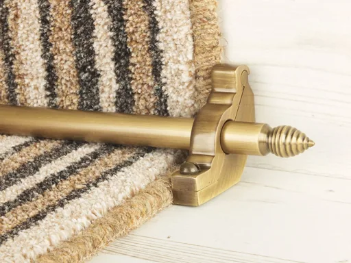 Antique brass stair rod with a beehive finial securing a neutral-toned striped carpet runner.