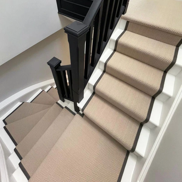 Beige chevron wool stair runner with dark binding on white stairs.