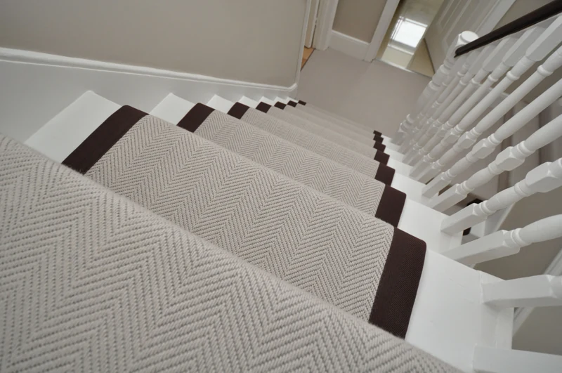 Beige herringbone carpet runner on white wooden stairs