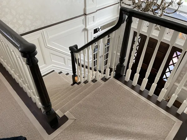 Beige herringbone stair runner on dark wood stairs.