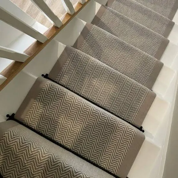 Beige herringbone stair runner with taupe border on white stairs.