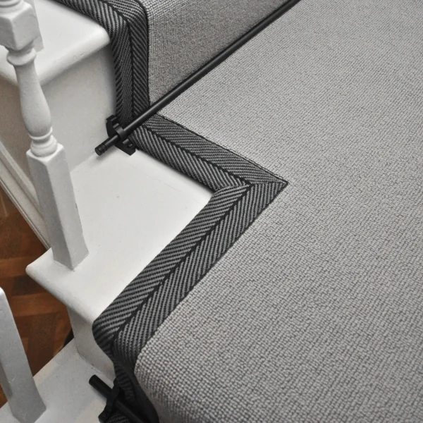 Black stair rods securing a grey runner with a patterned black-and-grey border