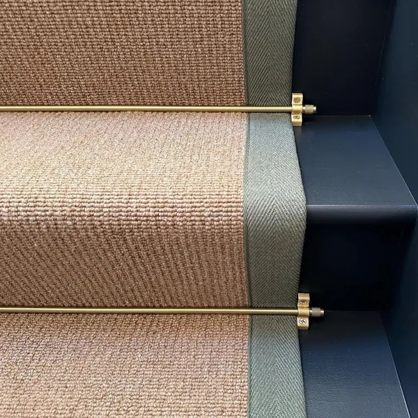 Brass stair rods securing a woven runner on dark stairs.