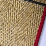 Close-up of oatmeal herringbone sisal stair runner with red edging.