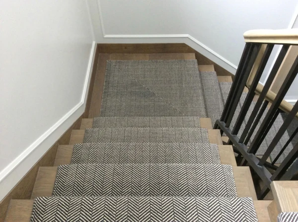 Dark grey herringbone stair runner on wood stairs.