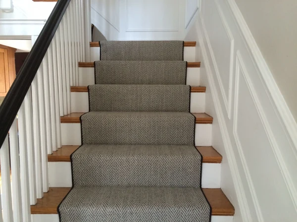 Grey herringbone stair runner with black binding on wood stairs.