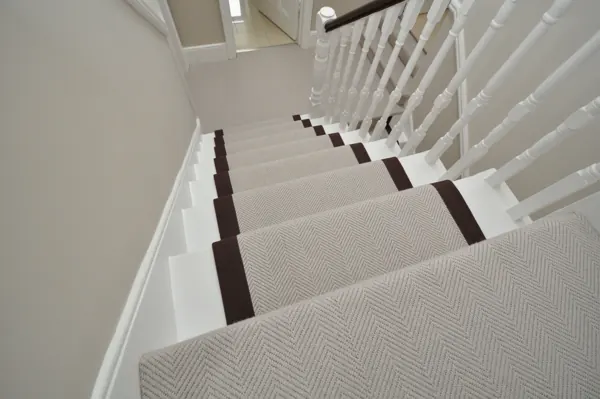 Grey herringbone stair runner with dark brown binding on white stairs.