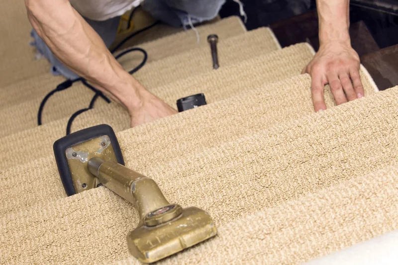 Installer stretching beige carpet onto wooden stairs