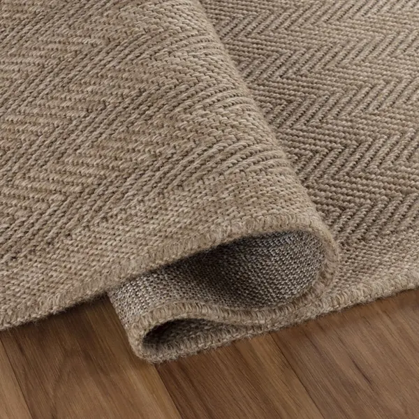 Natural jute herringbone rug rolled up on wood floor.