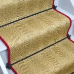 Oatmeal herringbone sisal stair runner with red edging and black stair rods.