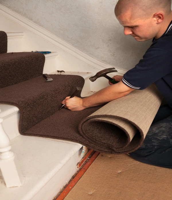 Tradesman securing dark brown carpet runner to stair