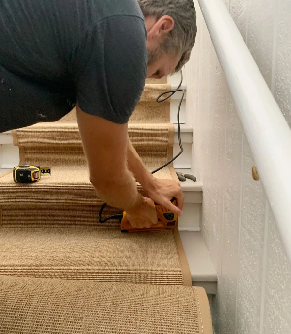 Stapling beige carpet runner to wooden stair riser
