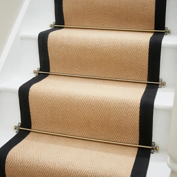 Tan herringbone stair carpet with black borders and brass rods.