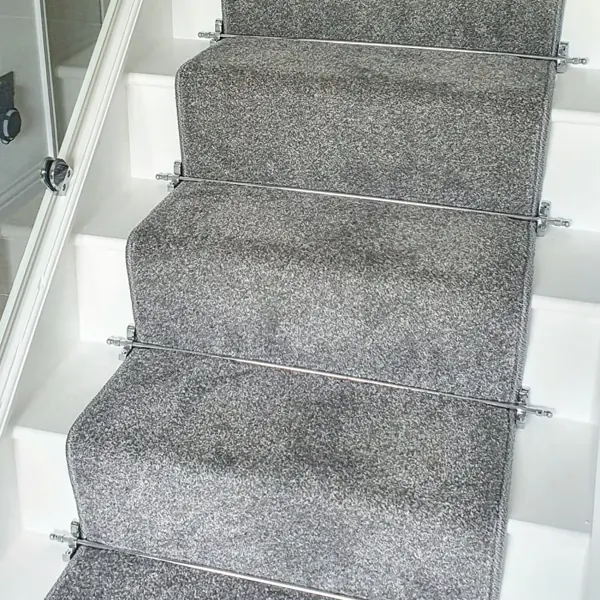 Textured grey carpet runner secured with silver stair rods on white stairs