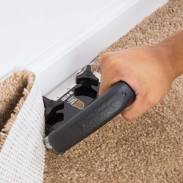 Trimming excess carpet along baseboard with wall trimmer