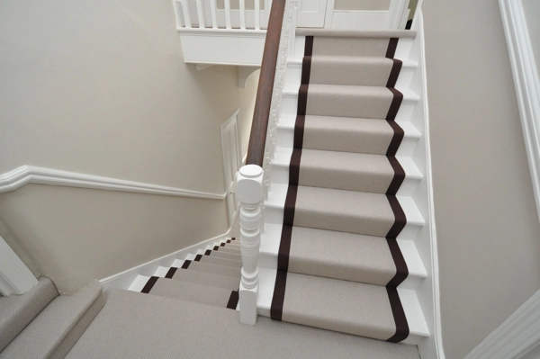 herringbone patterned wool stair runner with brown borders on white painted stairs.