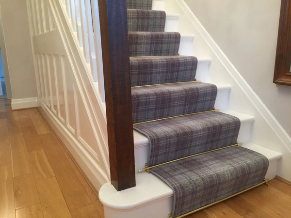 stair runner with brass stair rods installed on white painted wooden stairs.